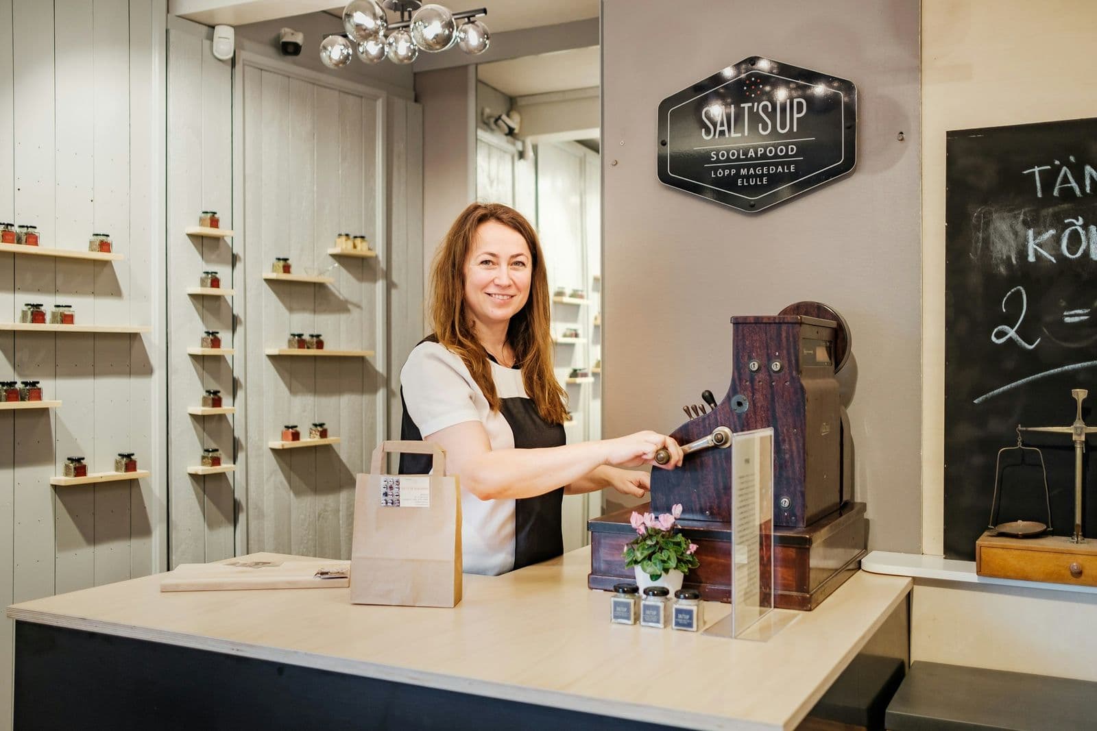 A shop owner smiling at the till behind the counter of her store